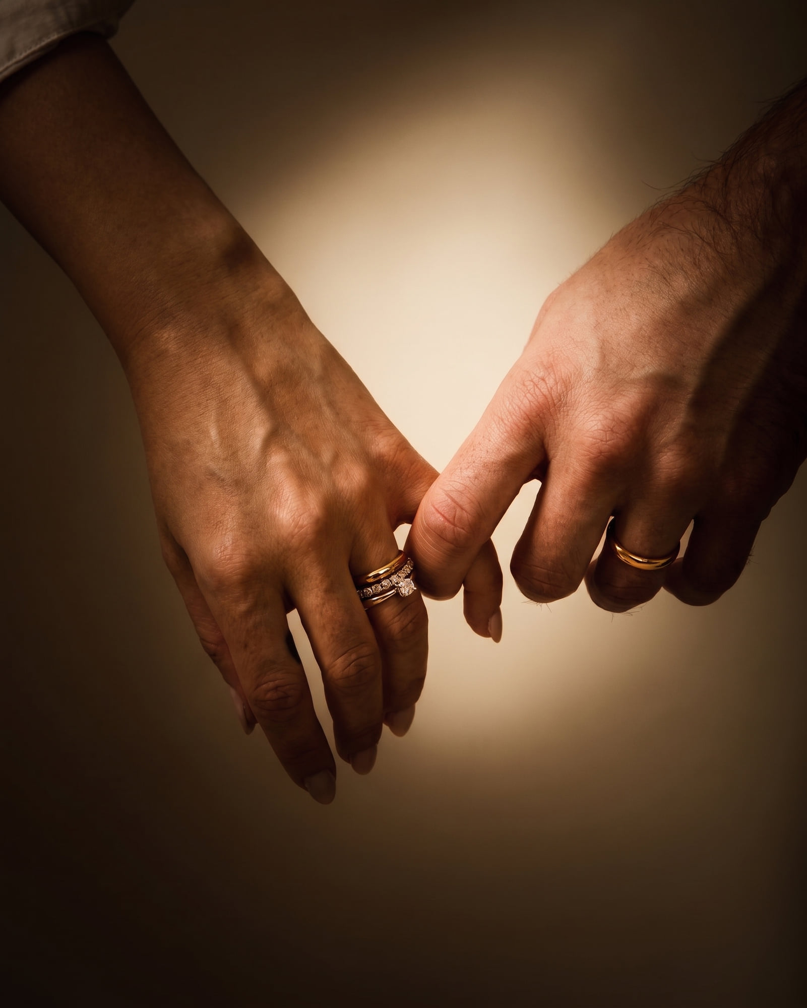 Mãos de casal com os mindinhos entrelaçados, alianças e solitário em ouro